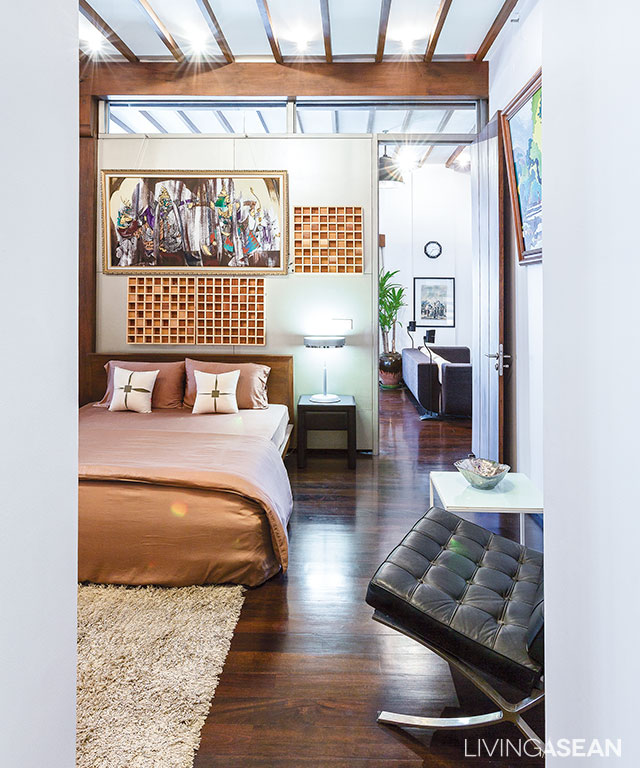 The bedroom’s white interior contrasts with dark brown colors of wood beams, posts, and ceiling joists.