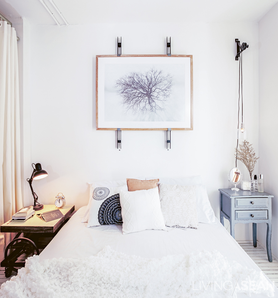 The queen-size bed and bedclothes are in shades of white to keep the tiny space from seeming cramped. A little panache is thrown in with the two bedside tables of different styles.