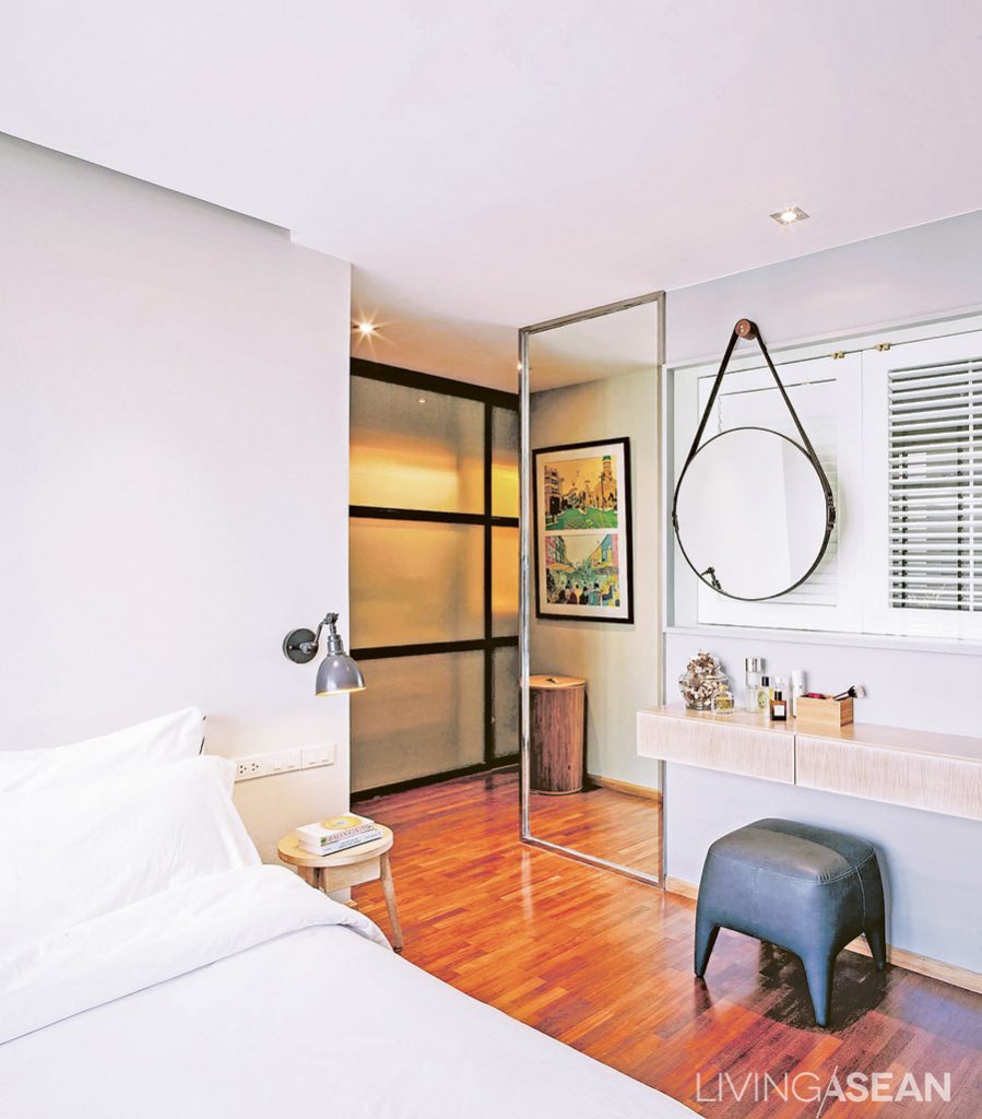 The clean and orderly bedroom connects to a dressing room. The black metal doorframes go well with the other parts of the home. Large glass pane along the corridor makes the space look wider and more open.