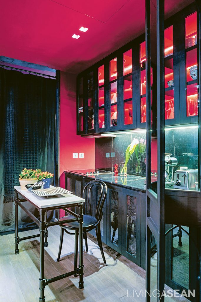 The pantry is striking. With its red wall and ceiling and multicolor drapes, the dark metal Arabian-style partition setting it off from the rest of the home. 