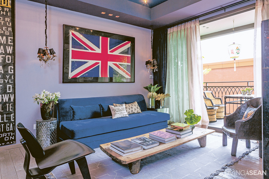 Dark colors alternate with paler ones, giving dimension to the "living room." The light gray wall is adorned with framed pictures. The teakwood floor is polished to a lighter shade, contrasting with the dark ceiling, and opens out onto the balcony, with its set of wicker chairs.