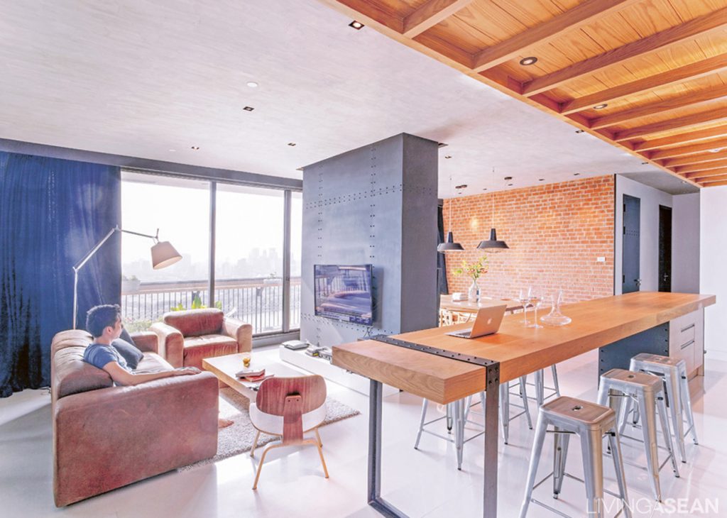 The living room is an open space that connects to everything else, the result that the owner was looking for. A TV-mounted wall made of black sheet metal separates the parlor from the dining area with brickwork in the background.