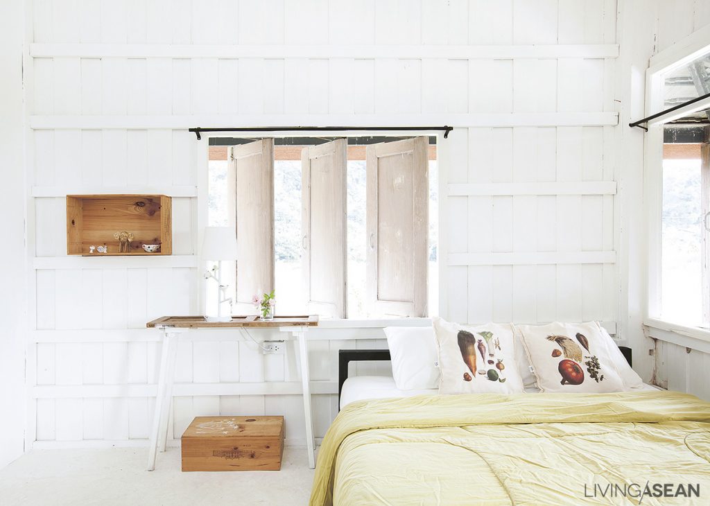 The bedroom is simple, uncluttered and set entirely in cool-toned whites. Wood boxes in the recessed wall and on the floor provide extra storage space.
