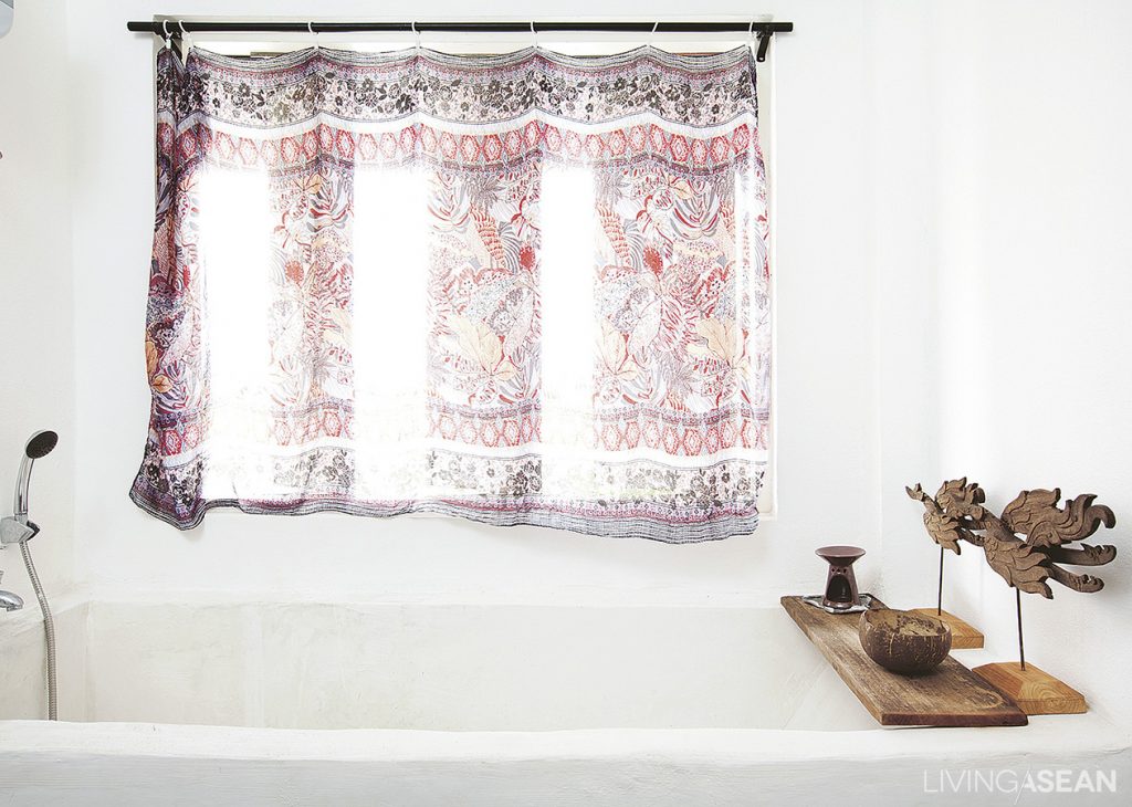 The bathtub is crafted on site using white cement. For privacy, the window is hung with a blind made out of handwoven ethnic fabrics.