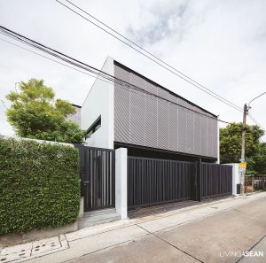 Tall aluminum latticework that makes the front façade protects the west-facing home from harsh sunlight. It provides a buffer against solar heat gain building up in the interior. On the street, black iron lattice fencing promotes natural air circulation and doubles as a privacy screen.